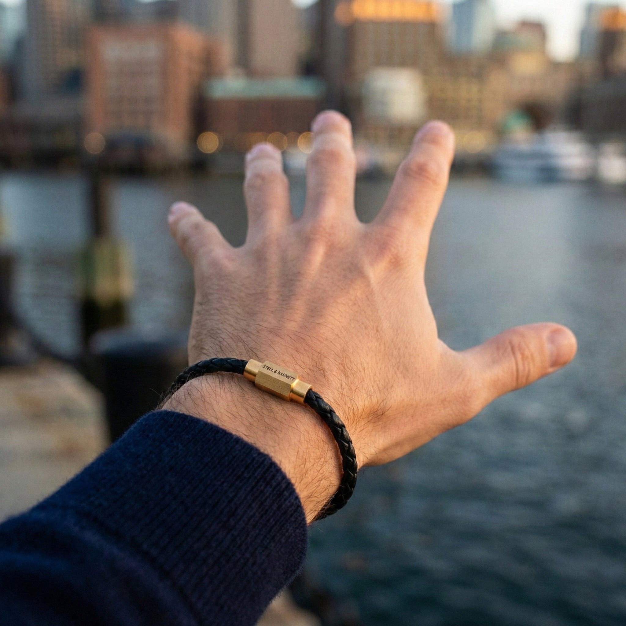 Black braided leather men’s bracelet with plated 18K gold clasp worn on wrist by the water