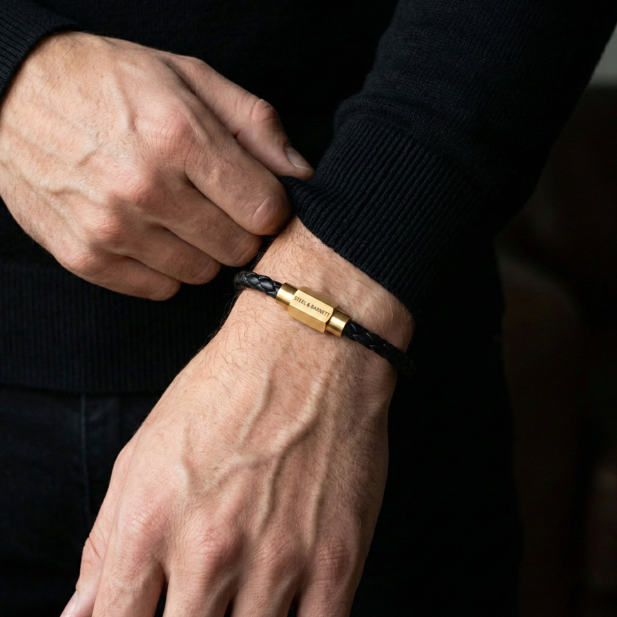 Black braided leather men’s bracelet with plated 18K gold clasp worn on wrist in close up