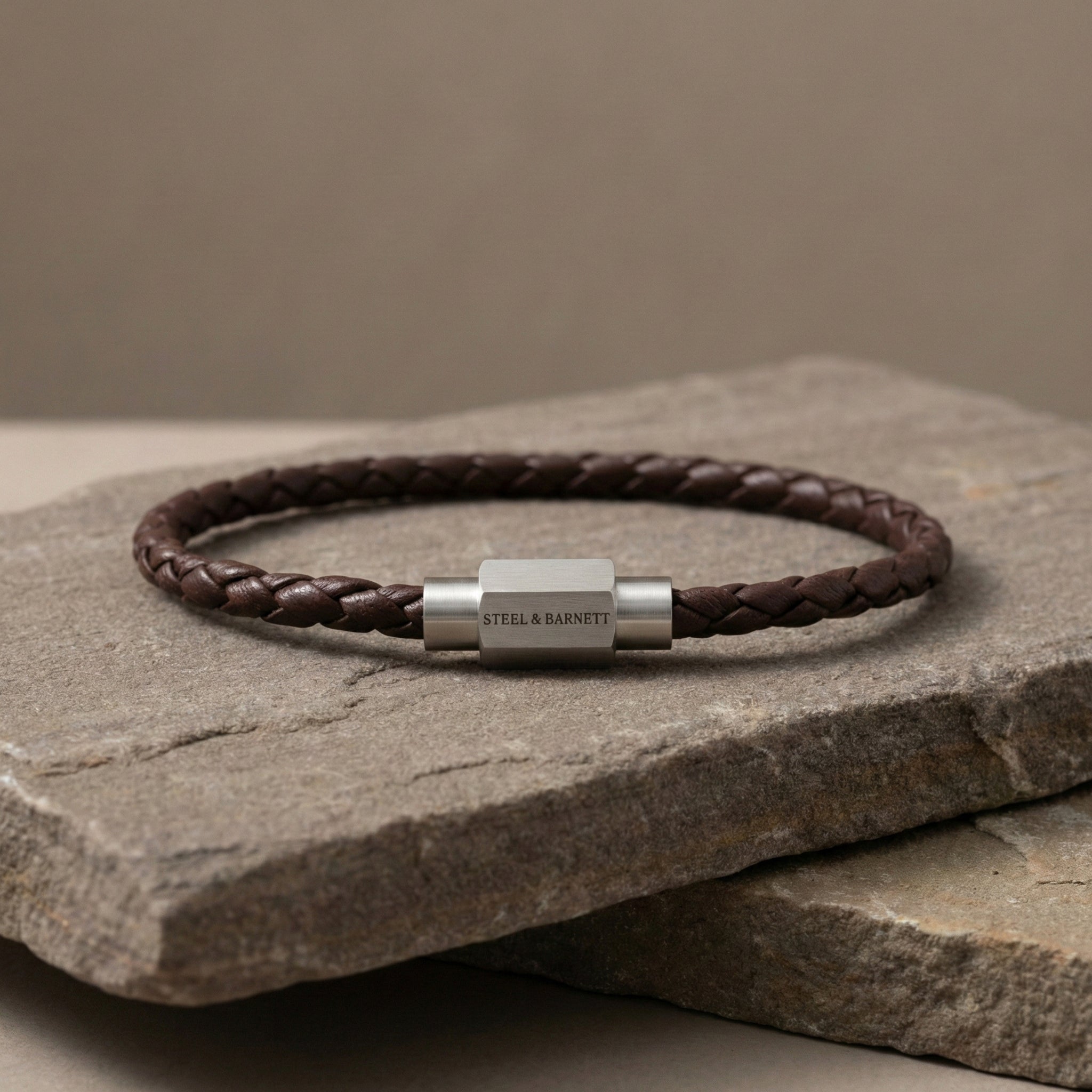 Brown braided leather men’s bracelet with brushed stainless steel magnetic clasp on stacked stone surface