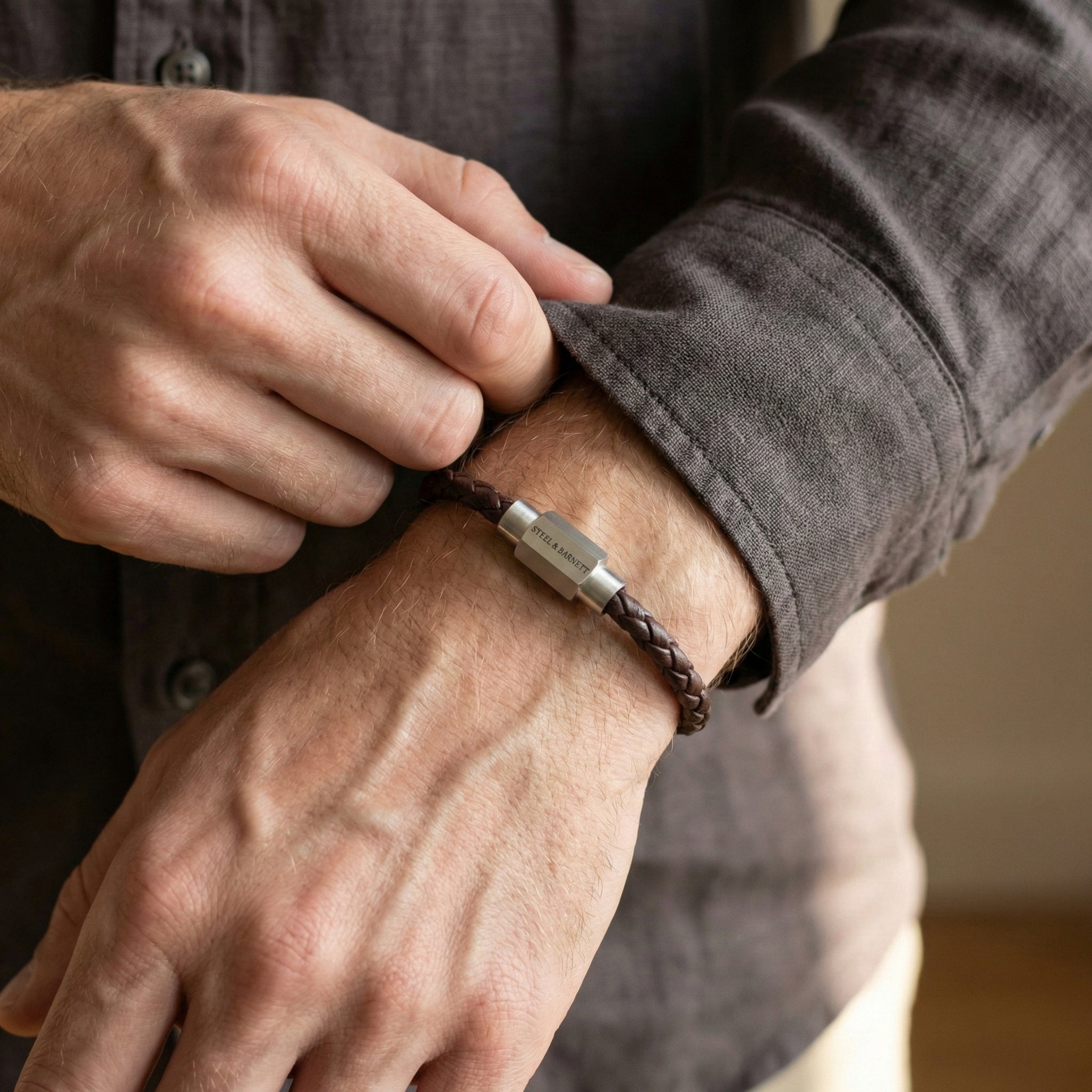 Brown braided leather men’s bracelet with brushed stainless steel clasp worn on wrist in lifestyle setting