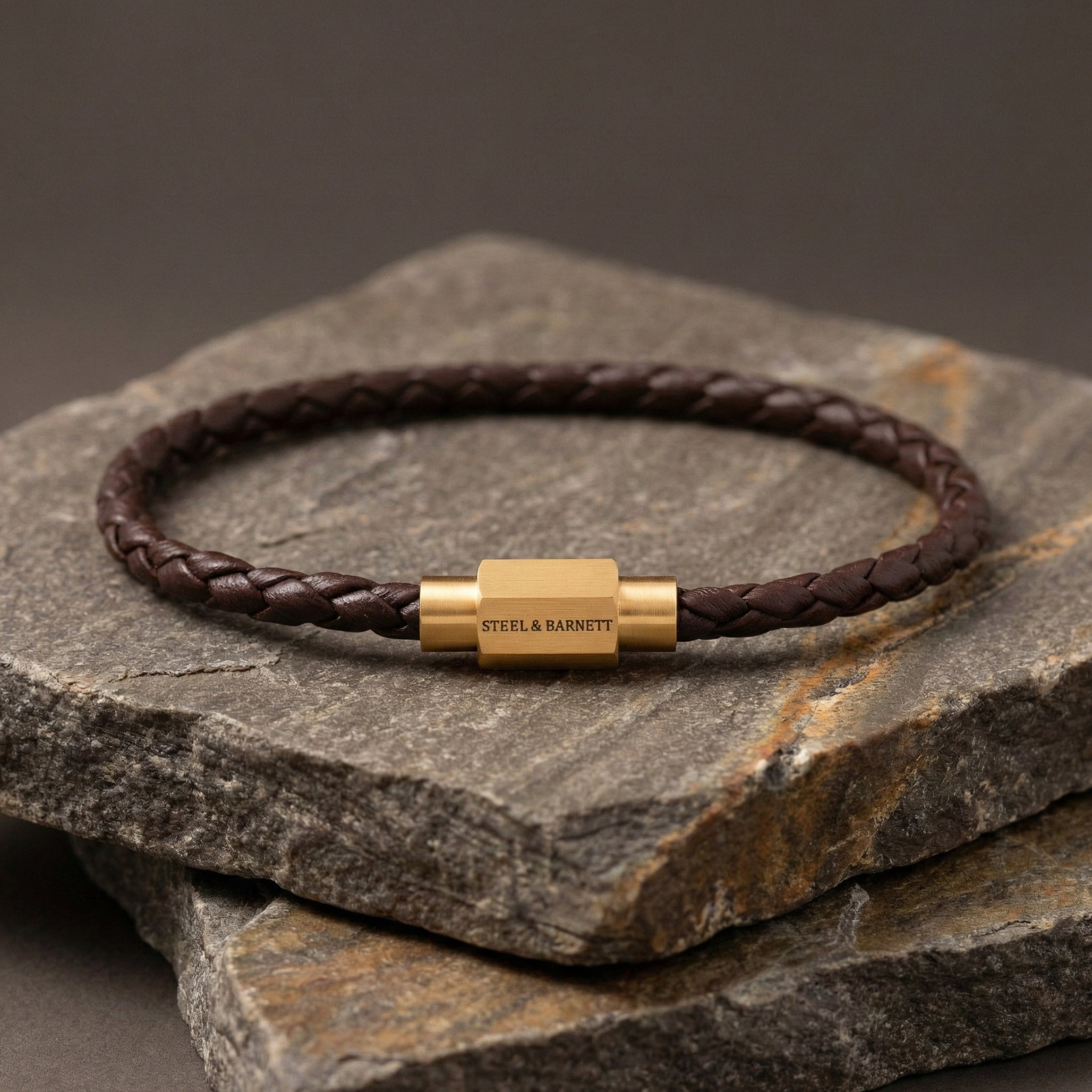 Brown braided leather men’s bracelet with plated 18K gold clasp on stacked stone surface