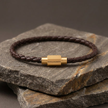Brown braided leather men’s bracelet with plated 18K gold clasp on stacked stone surface