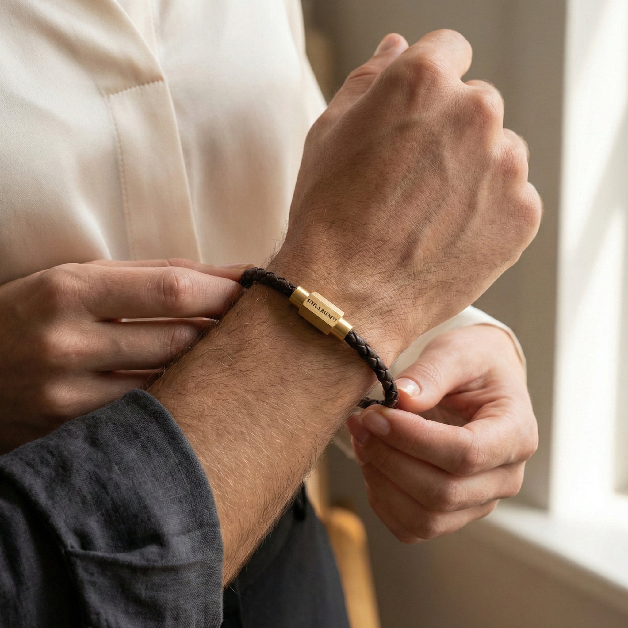 Brown braided leather men’s bracelet with plated 18K gold clasp worn on wrist in lifestyle setting