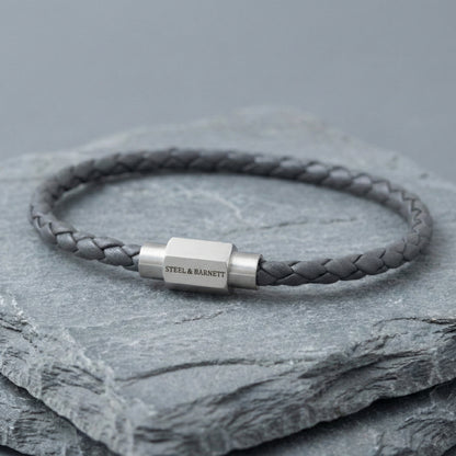 Grey braided leather men’s bracelet with brushed stainless steel clasp on stacked stone surface