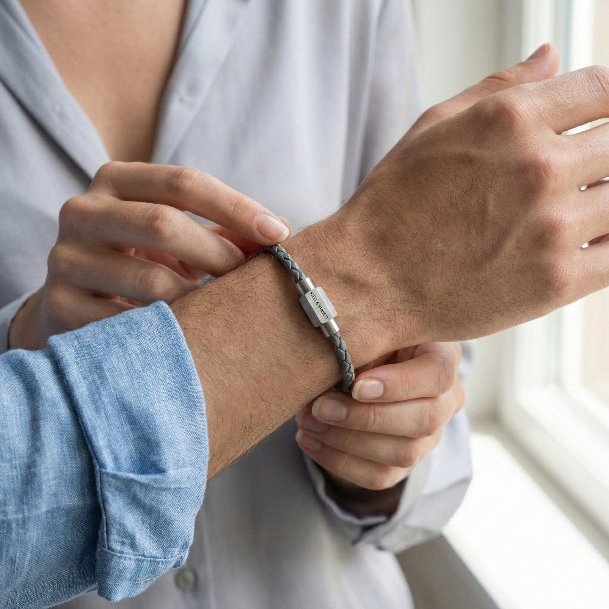 Grey braided leather men’s bracelet with brushed stainless steel magnetic clasp worn on wrist in lifestyle setting