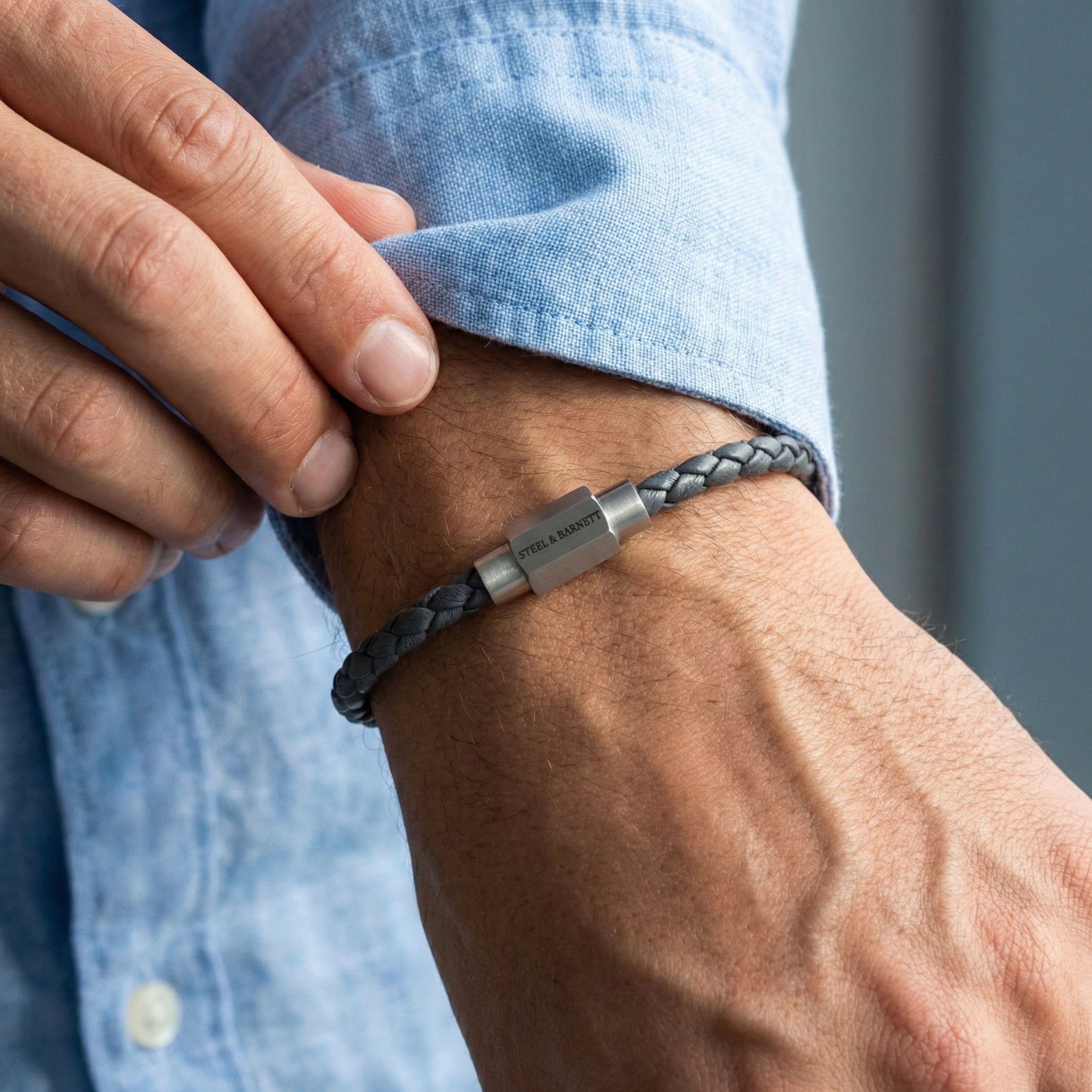 Grey braided leather men’s bracelet with brushed stainless steel magnetic clasp worn on wrist in close up