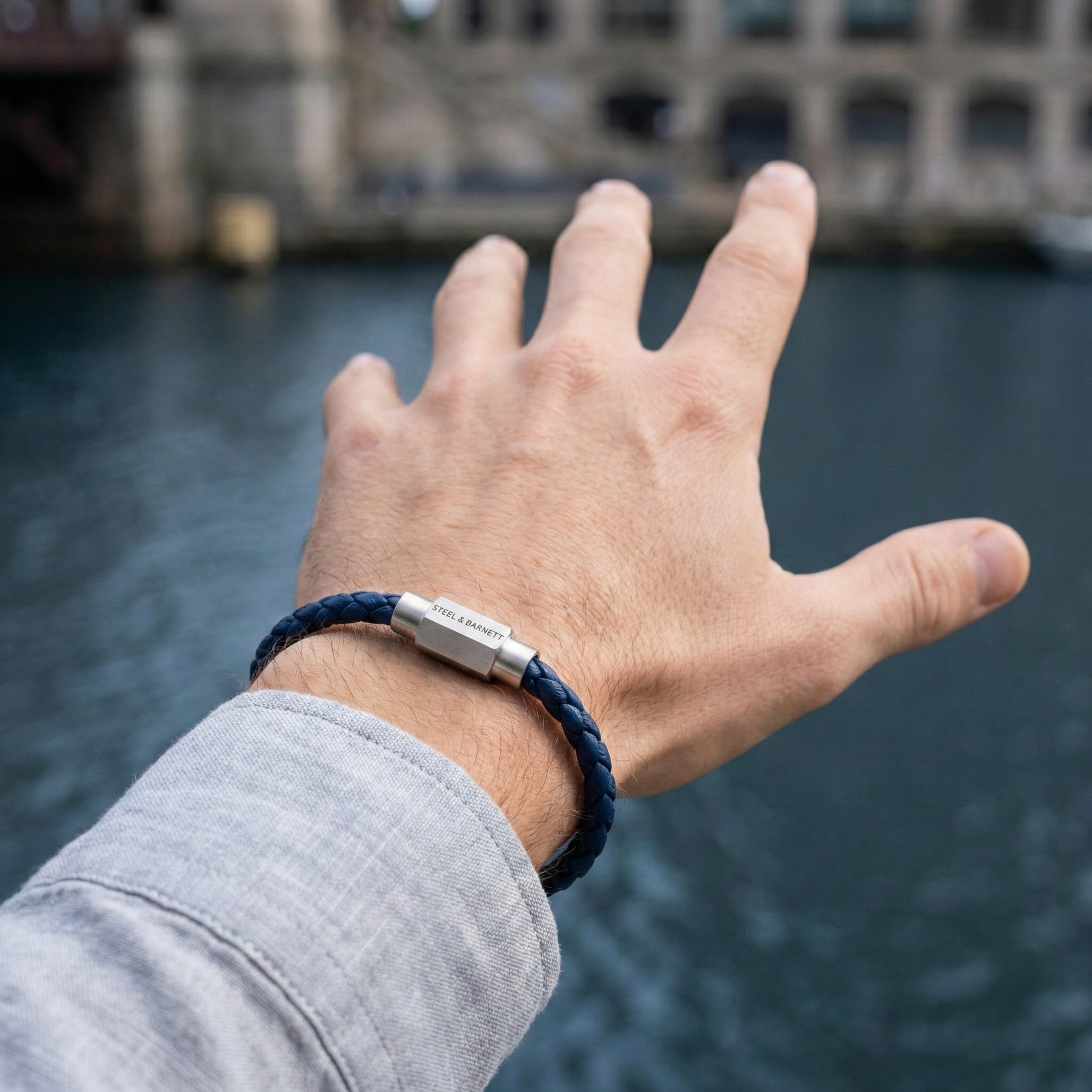 Blue braided leather men’s bracelet with brushed stainless steel magnetic clasp worn on wrist by the water