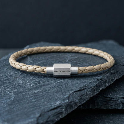 Beige braided leather men’s bracelet with brushed stainless steel clasp on a dark stone surface
