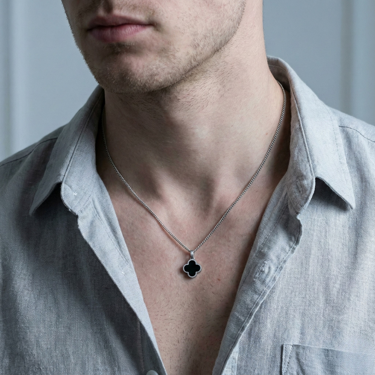 Men's stainless steel necklace with black clover pendant worn with an open collar shirt