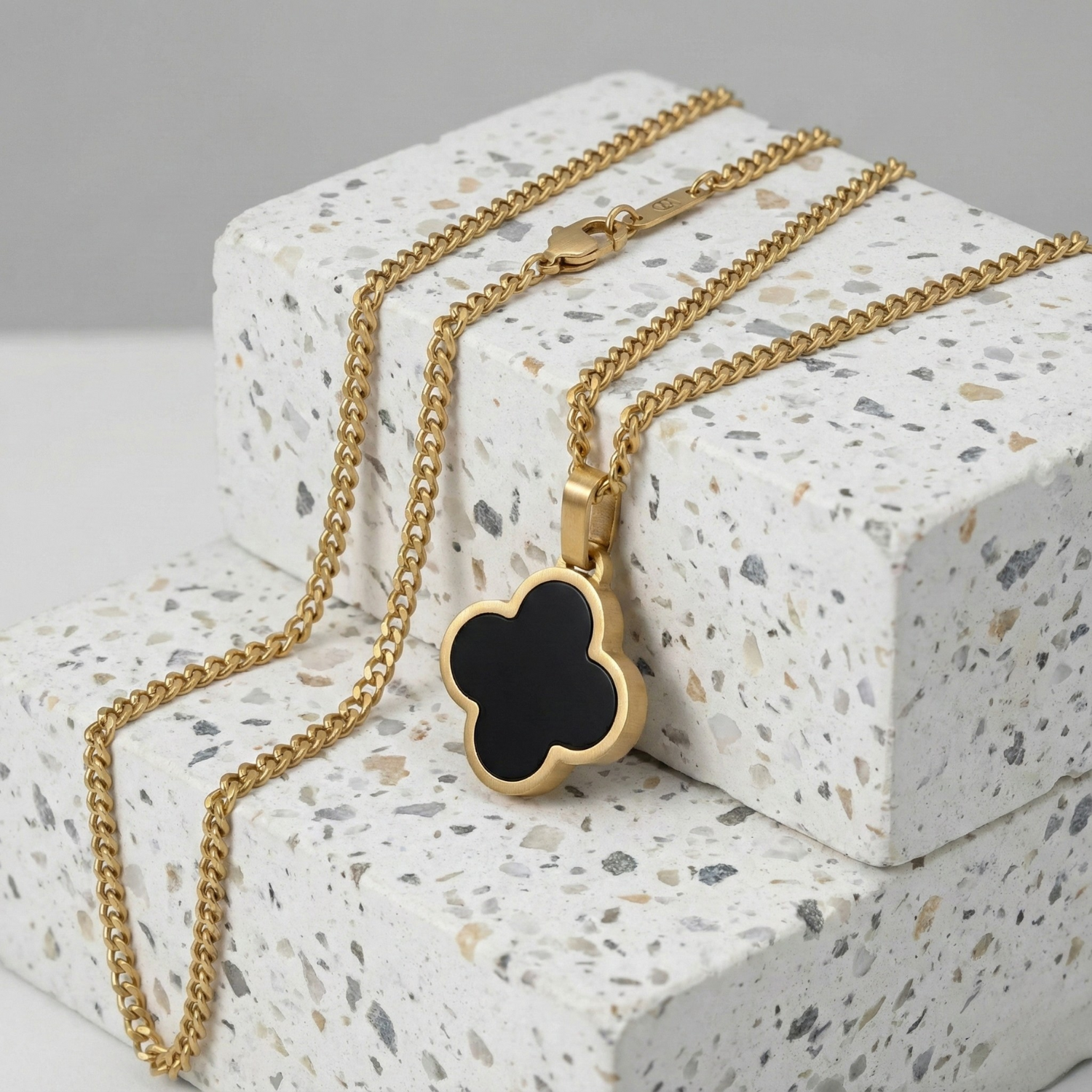 Gold necklace with a black clover pendant on a textured white surface