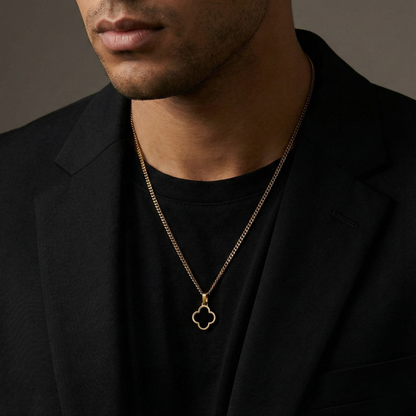 Man wearing a gold necklace with a clover pendant against a dark background
