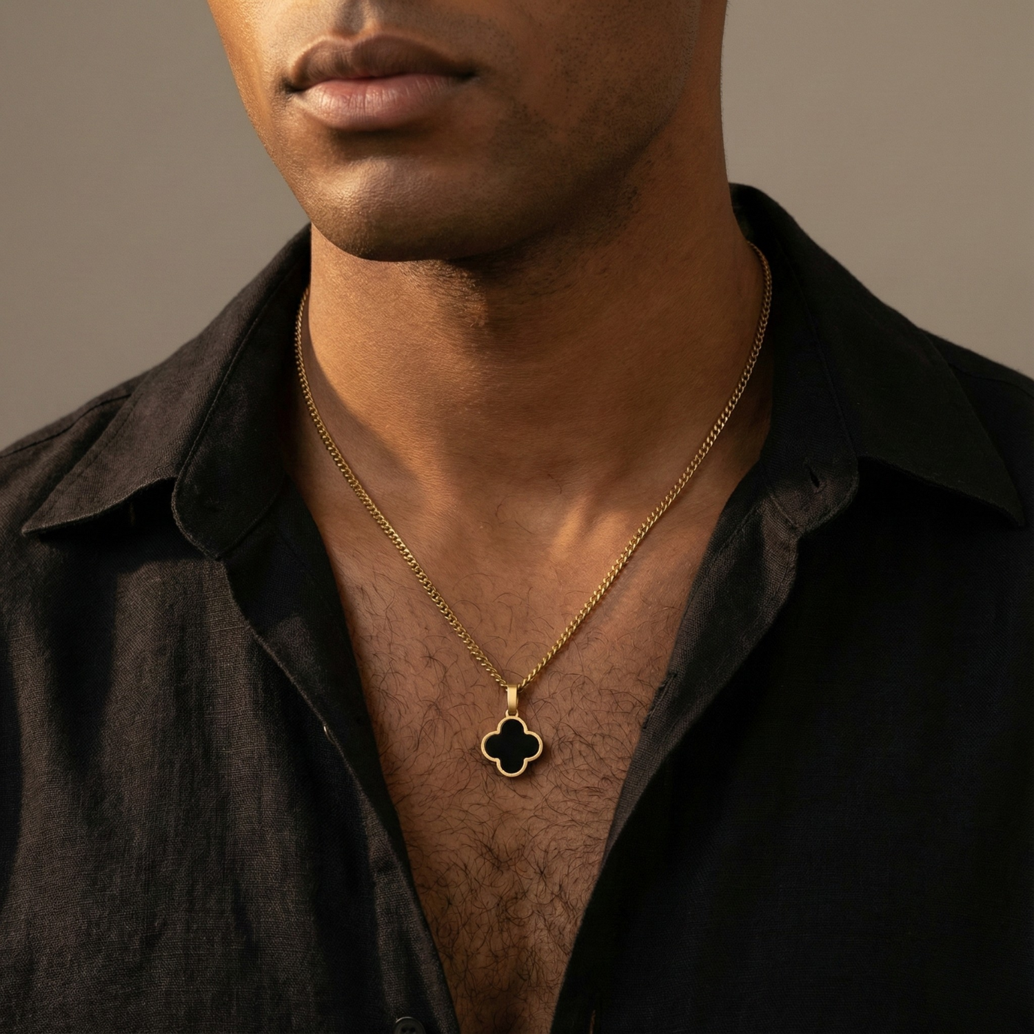 Man wearing a gold necklace with a clover pendant against a neutral background