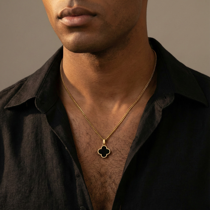 Man wearing a gold necklace with a clover pendant against a neutral background