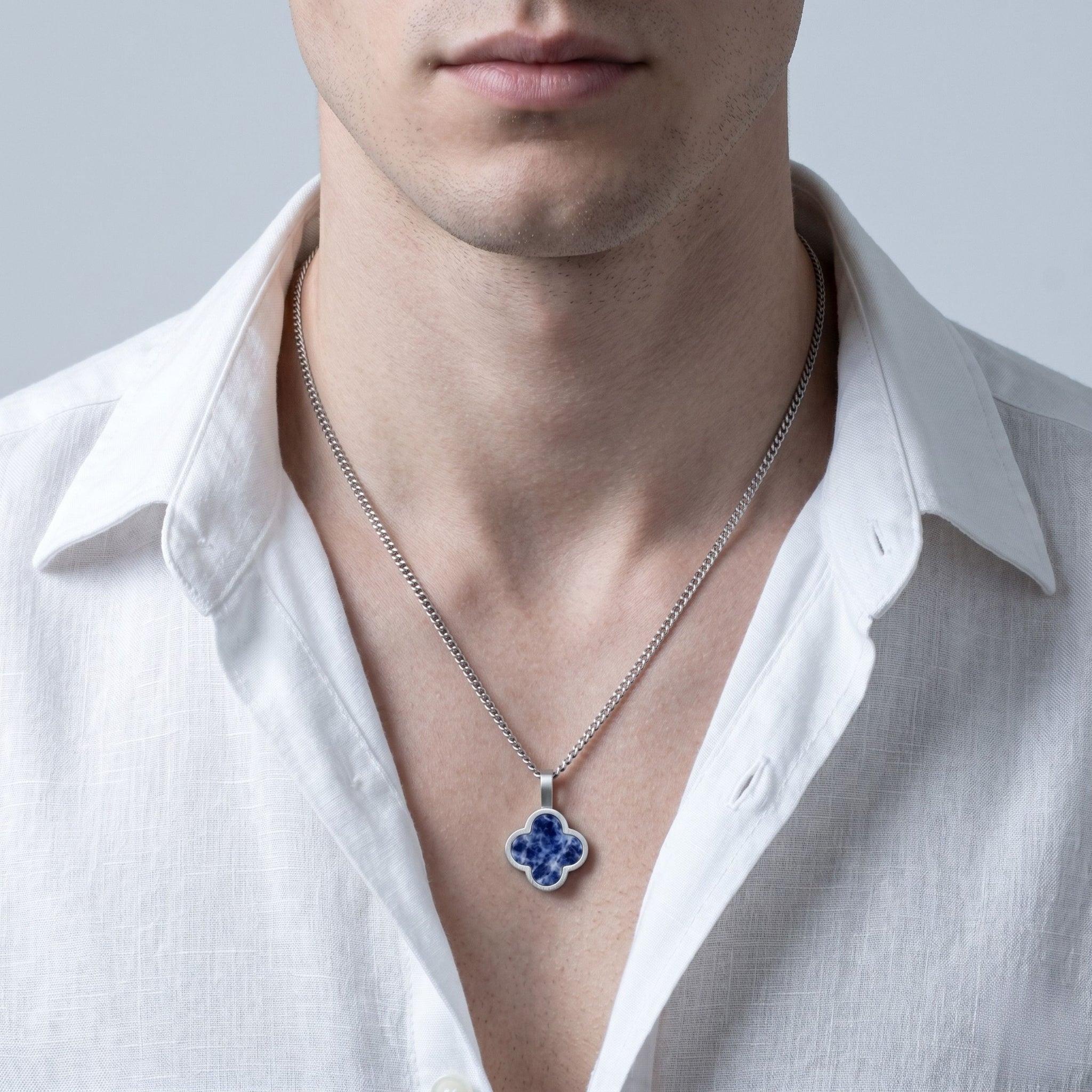 Man wearing a white shirt with a silver necklace featuring a blue sodalite  pendant.