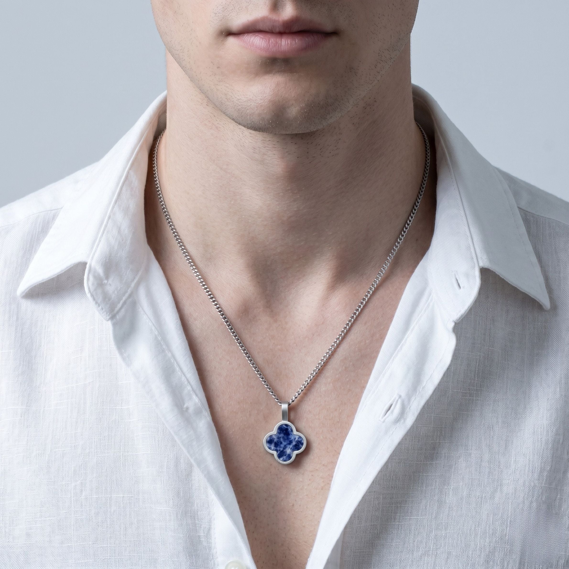 Man wearing a white shirt with a silver necklace featuring a blue sodalite  pendant.
