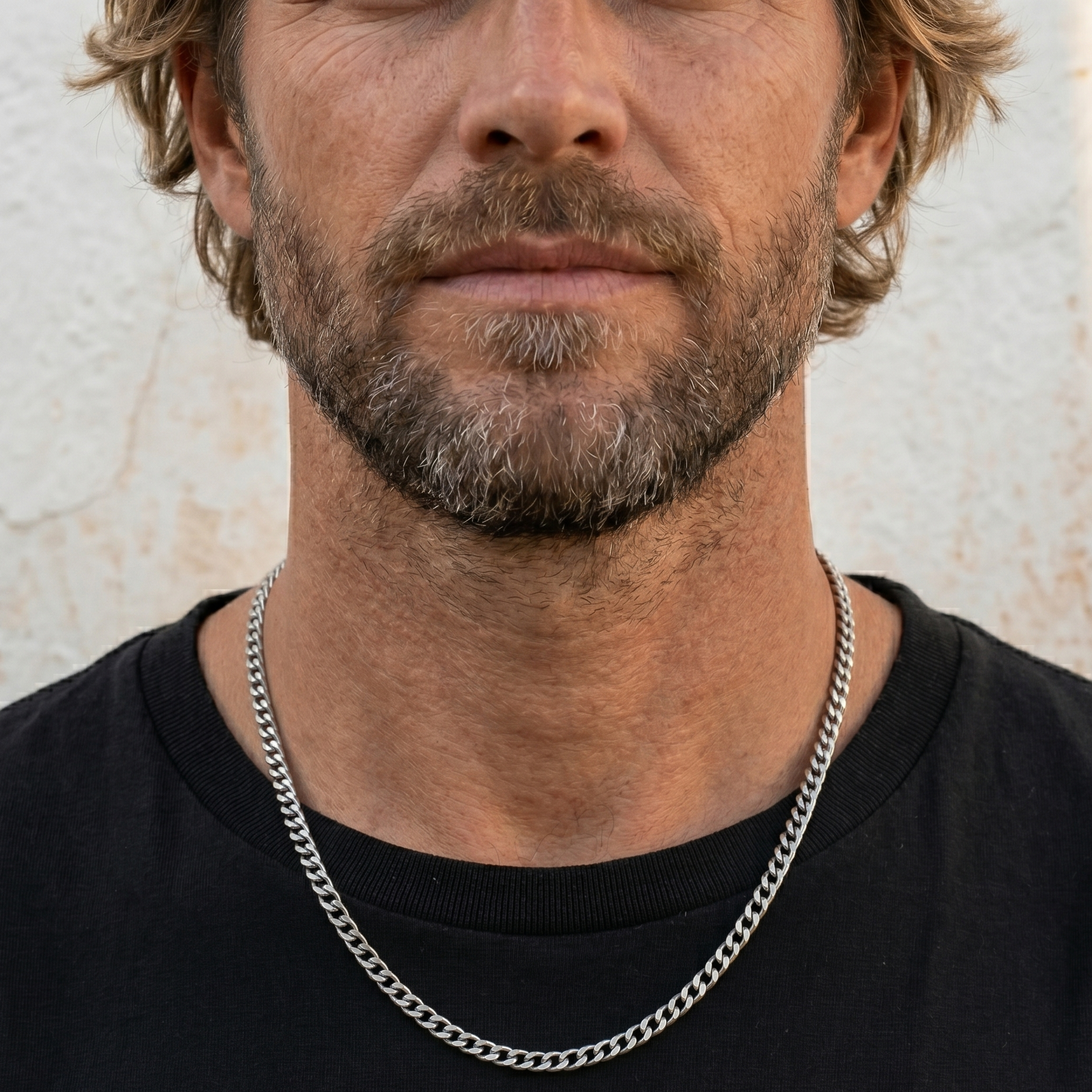 Man wearing a black shirt and silver chain necklace against a neutral background