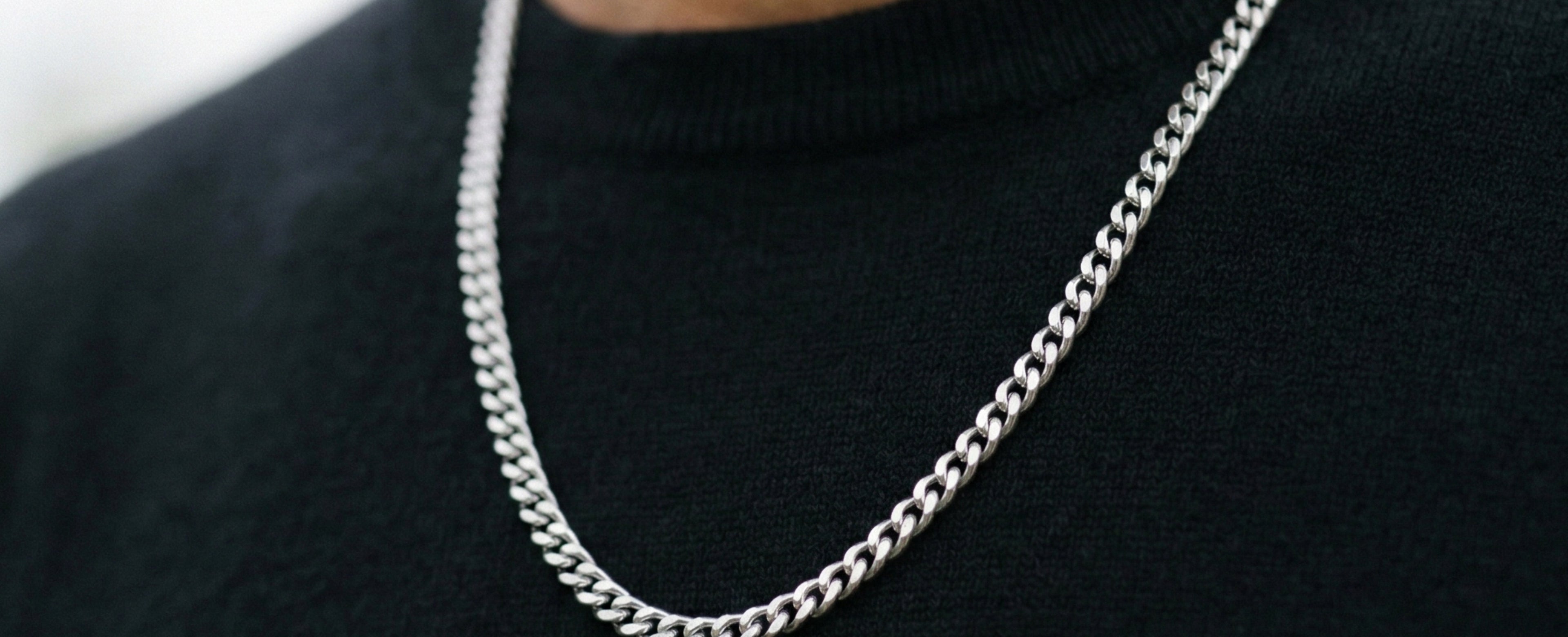 Stainless steel curb chain necklace for men with polished silver links worn around the neck over a black sweater in a close-up view