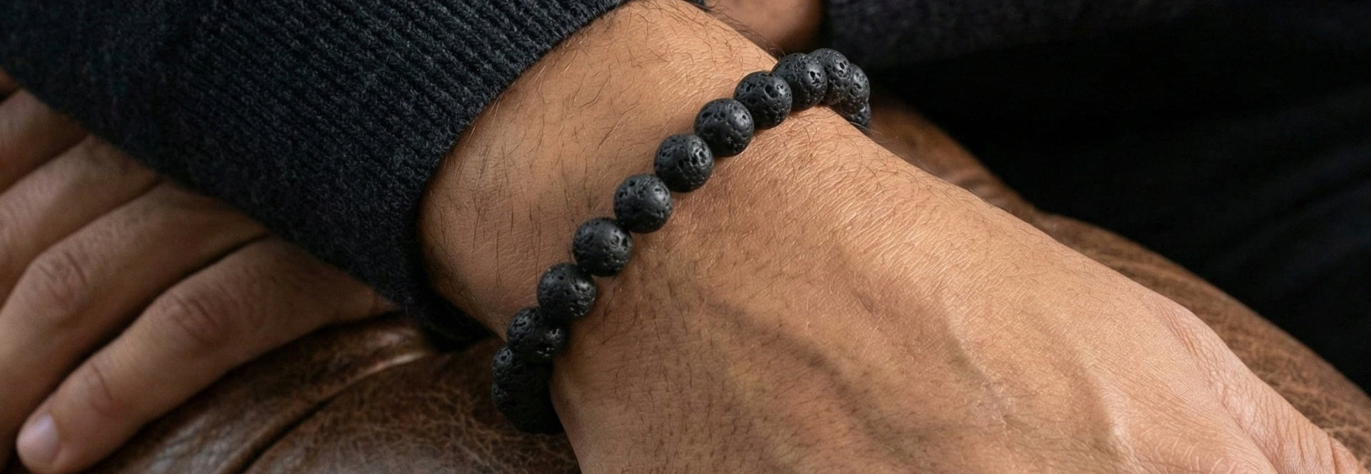 Black beaded men's bracelet with matte textured stone beads in a minimalist style worn on wrist against a brown leather surface
