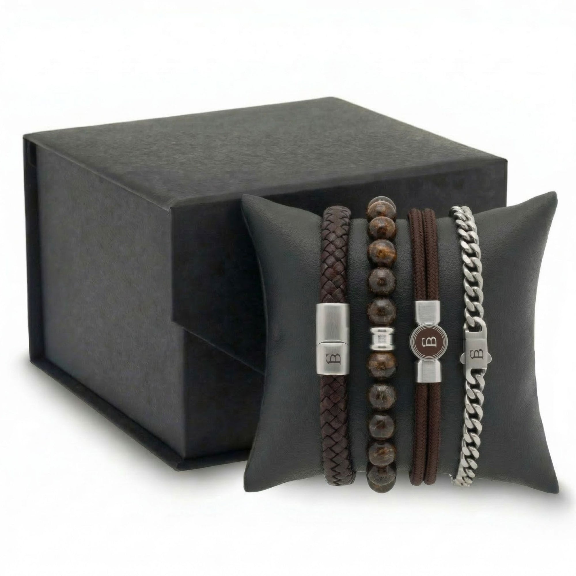 Stacked brown leather, beaded stone and stainless steel men's bracelet set with braided and chain styles on cushion beside gift box