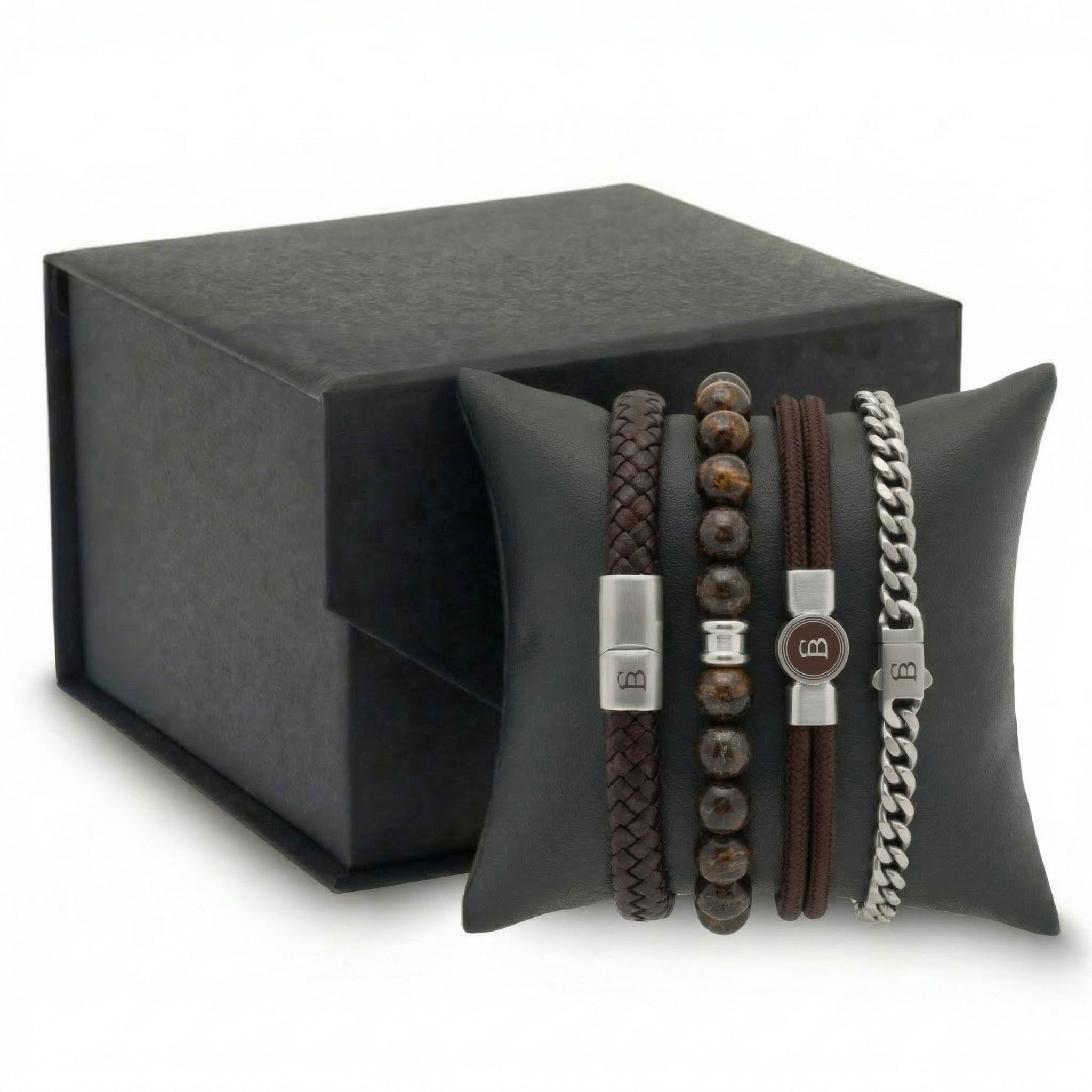 Stacked brown leather, beaded stone and stainless steel men's bracelet set with braided and chain styles on cushion beside gift box
