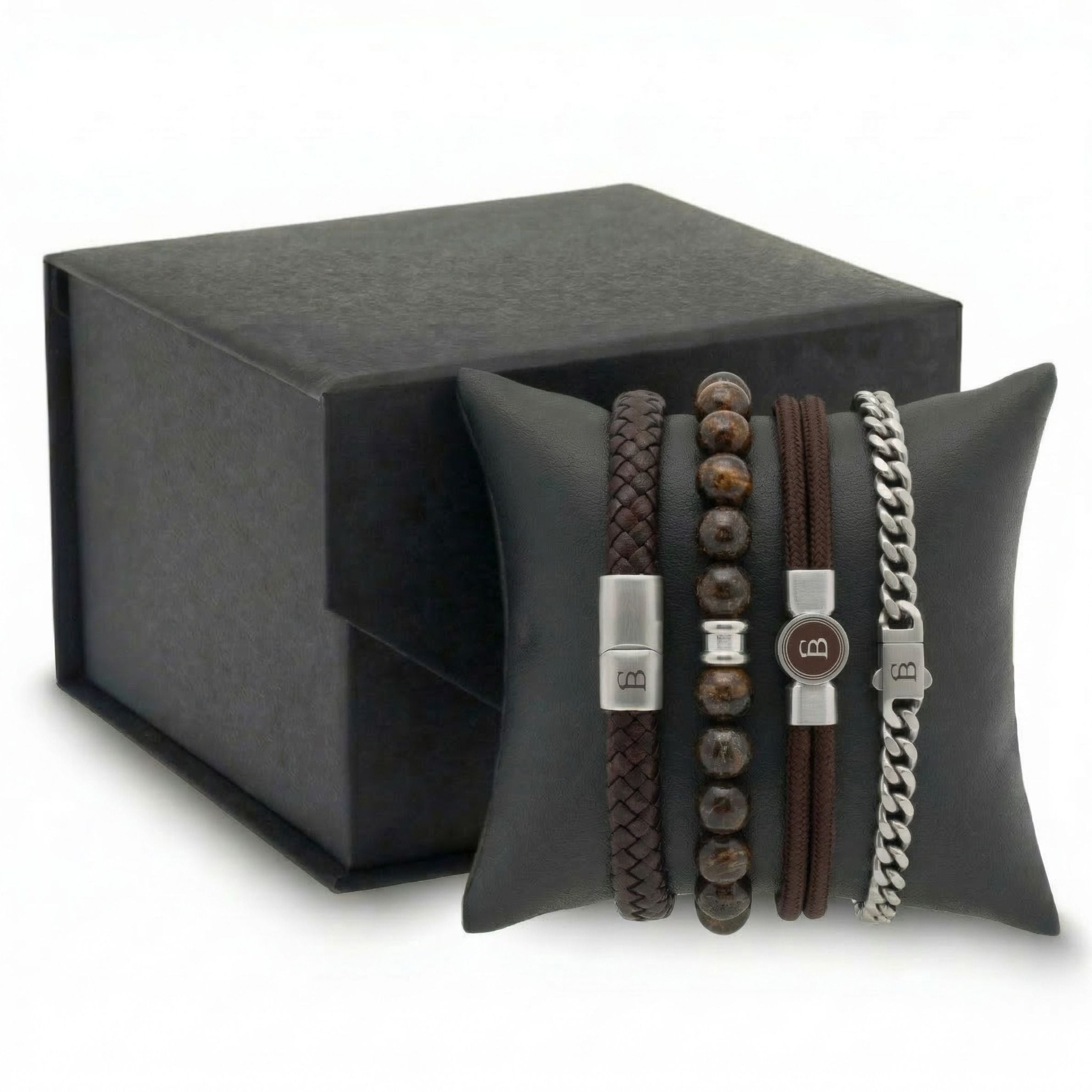 Stacked brown leather, beaded stone and stainless steel men's bracelet set with braided and chain styles on cushion beside gift box
