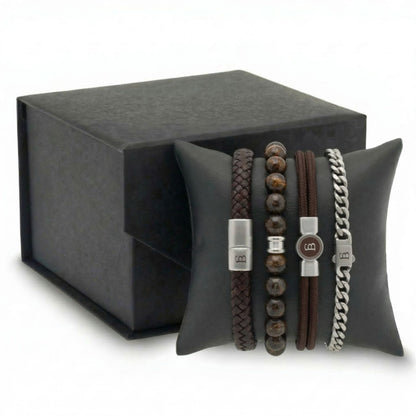 Stacked brown leather, beaded stone and stainless steel men's bracelet set with braided and chain styles on cushion beside gift box