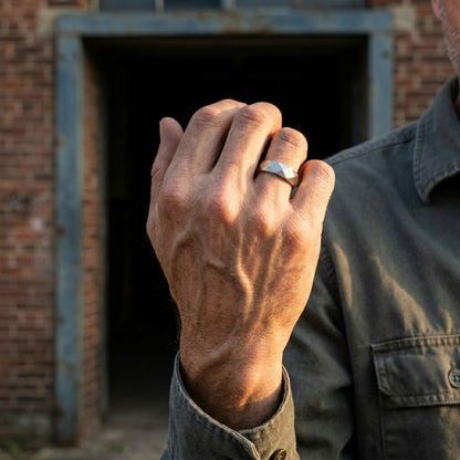 Silver geometric men's ring with a brushed finish worn on a hand in an industrial outdoor setting