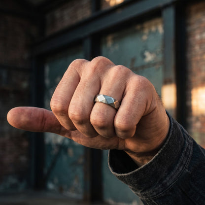 Brushed stainless steel men's ring with angular facets shown close up on a clenched hand outdoors