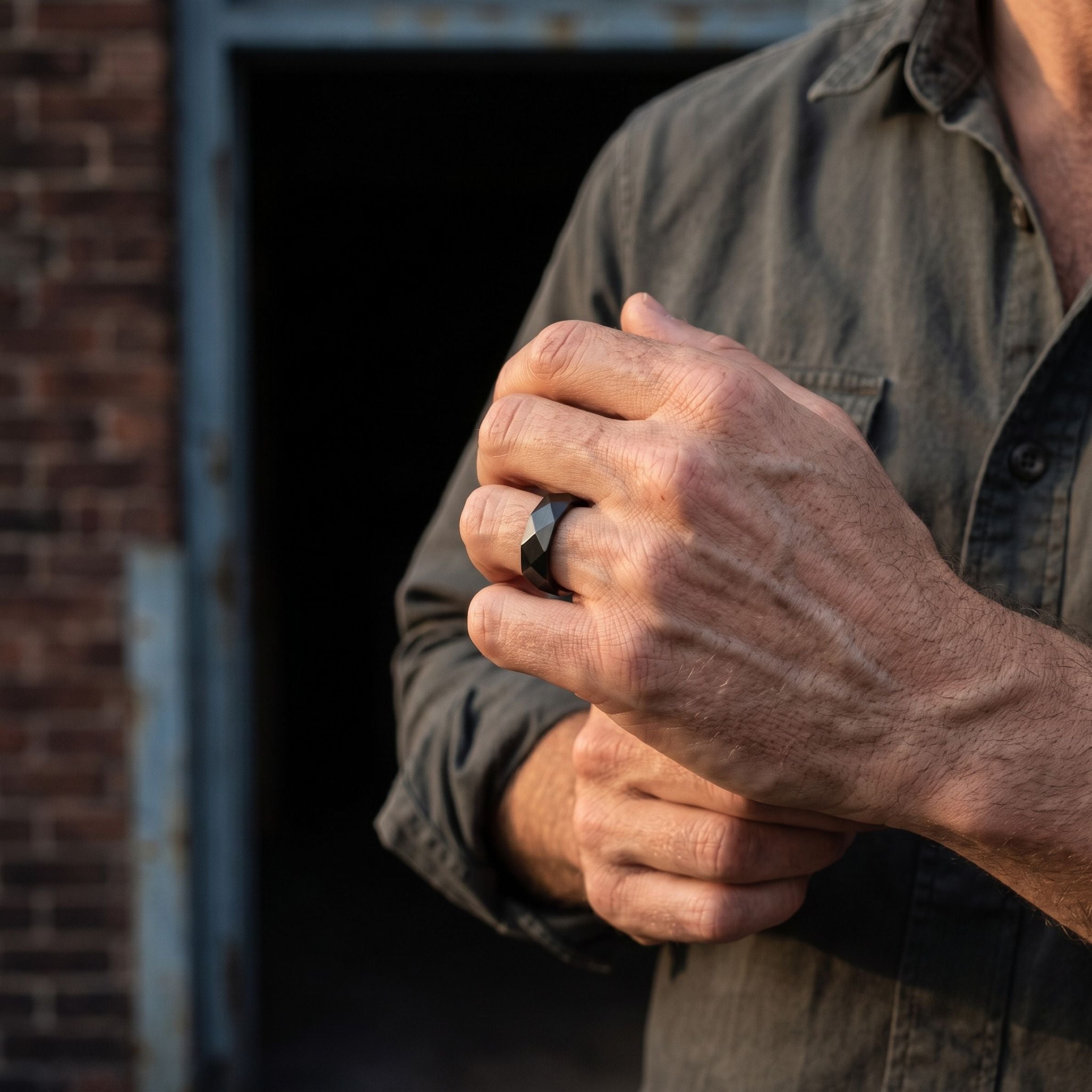 Black stainless steel men's ring with a faceted geometric finish worn on a hand in an outdoor lifestyle close up