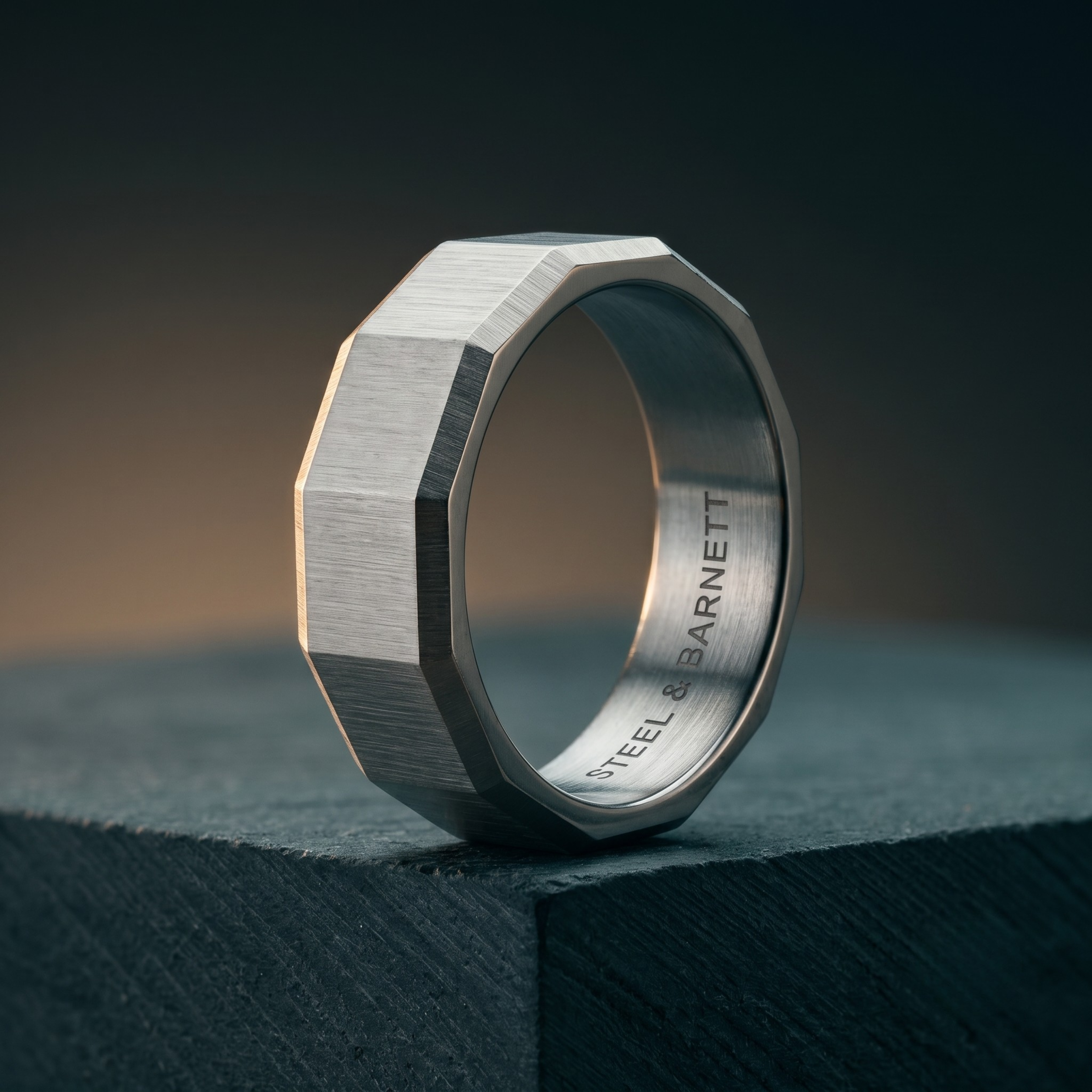 Silver stainless steel men's ring with a brushed geometric design displayed upright on a dark stone surface
