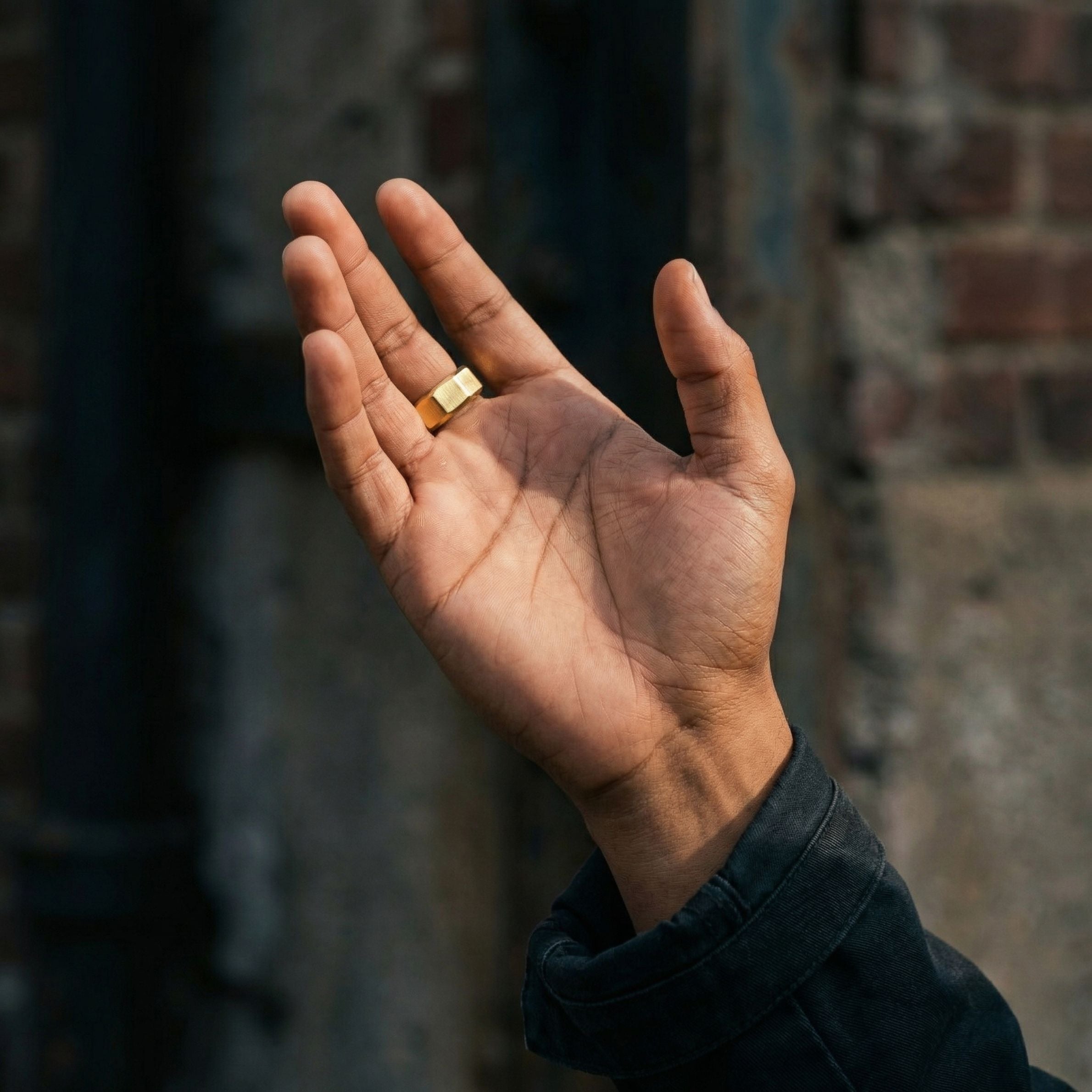 Gold stainless steel men's ring with a brushed geometric finish shown on an open hand in natural outdoor light