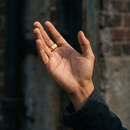 Gold stainless steel men's ring with a brushed geometric finish shown on an open hand in natural outdoor light