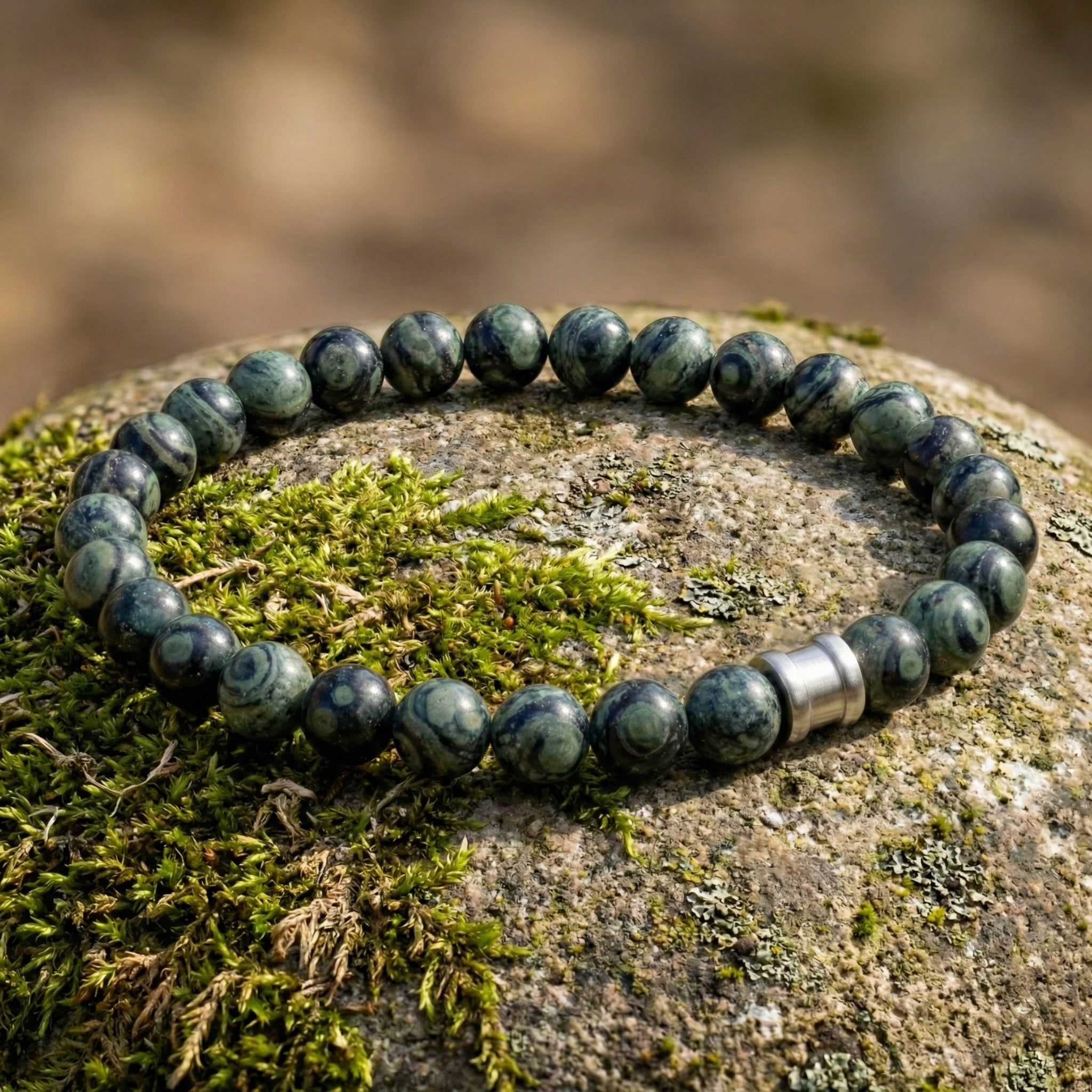 Green kambaba gemstone men’s bracelet with round polished beads and stainless steel accent on a moss covered stone