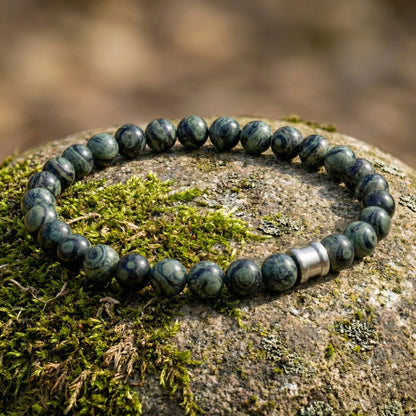 Green kambaba gemstone men’s bracelet with round polished beads and stainless steel accent on a moss covered stone