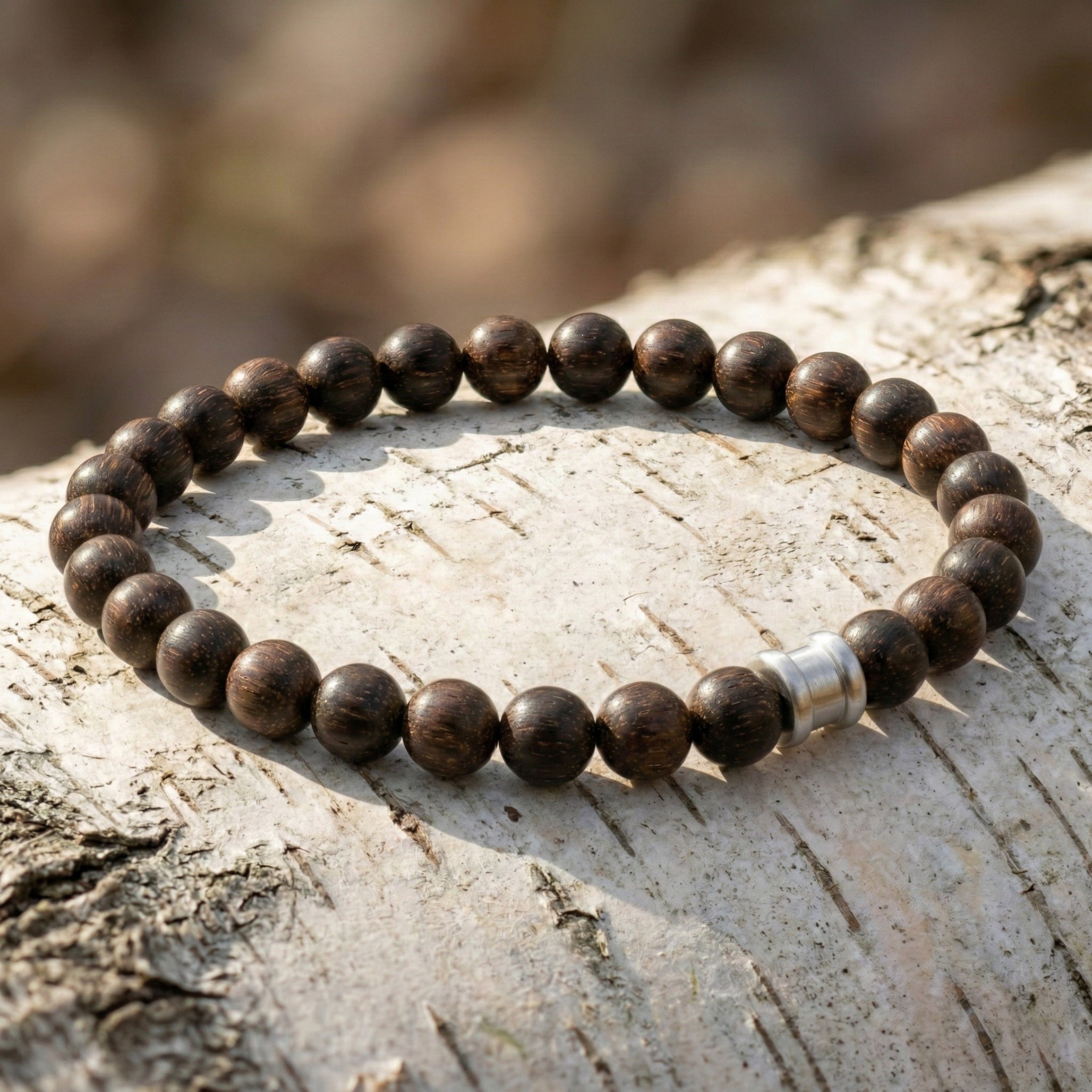 Dark brown wooden bead men’s bracelet with round matte beads and stainless steel accent on a light wood surface