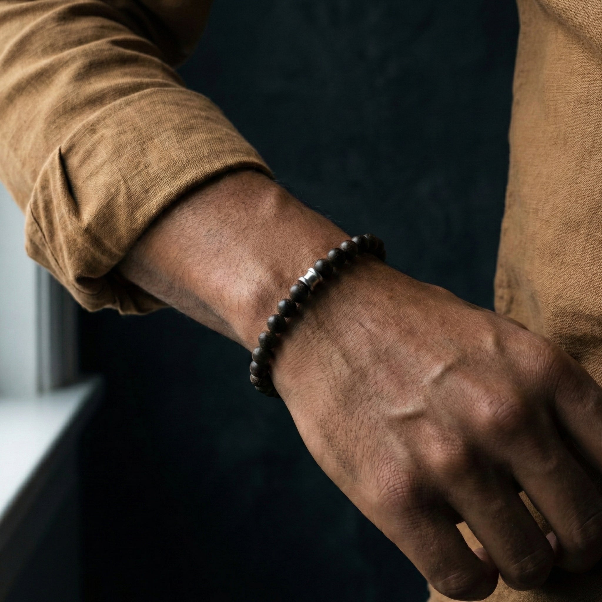 Dark brown wooden bead men’s bracelet with round matte beads worn on wrist in a lifestyle setting