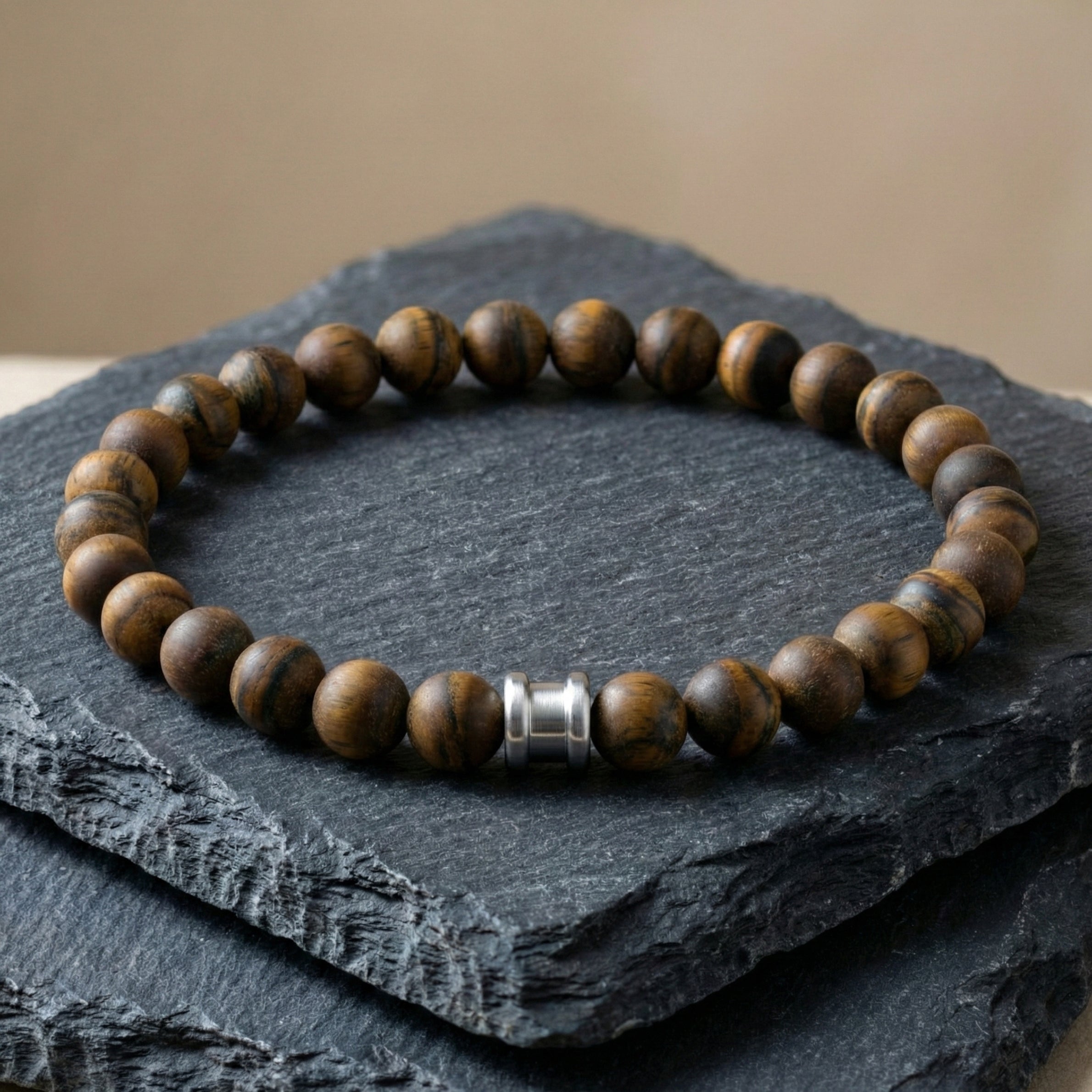 Brown tiger eye men’s bracelet with round matte beads and stainless steel accent on a dark slate surface