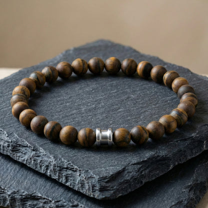 Brown tiger eye men’s bracelet with round matte beads and stainless steel accent on a dark slate surface