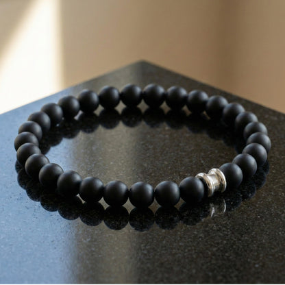 Black onyx men’s bracelet with round matte gemstone beads and stainless steel accent on a dark stone surface