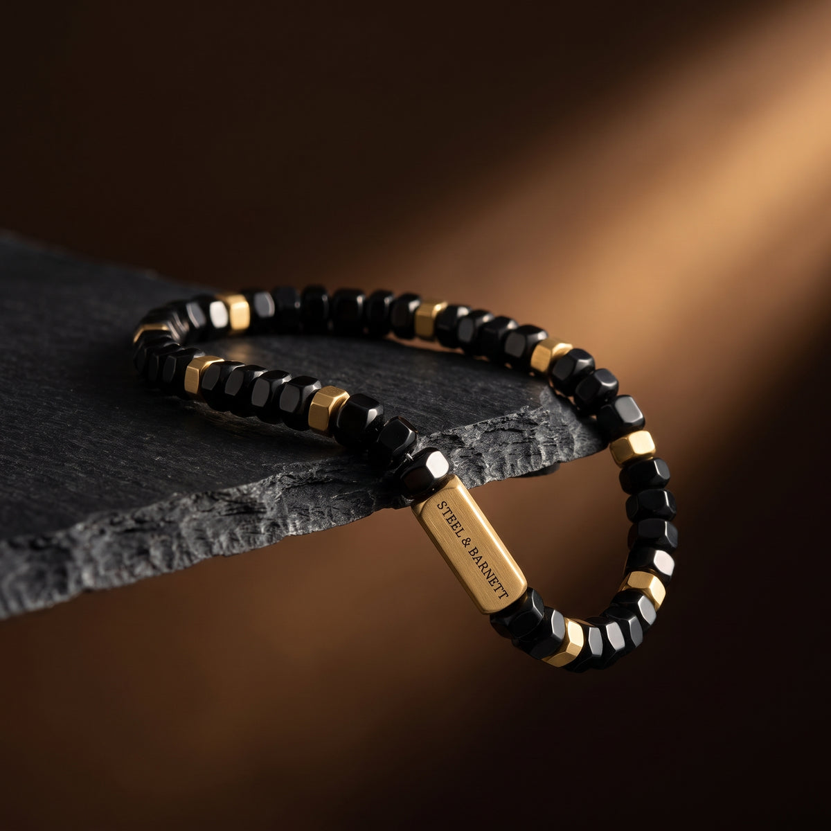 Black faceted bead men's bracelet with plated 18K gold accents arranged on a dark textured stone surface