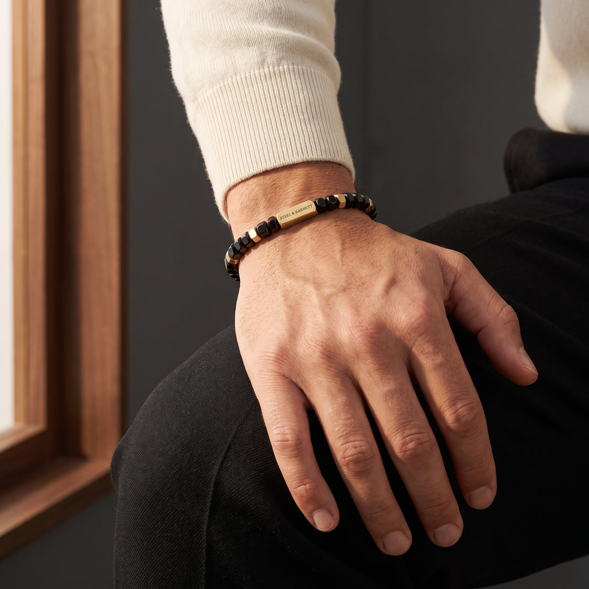 Black faceted bead men's bracelet with plated 18K gold clasp and accents worn on the wrist in warm natural light