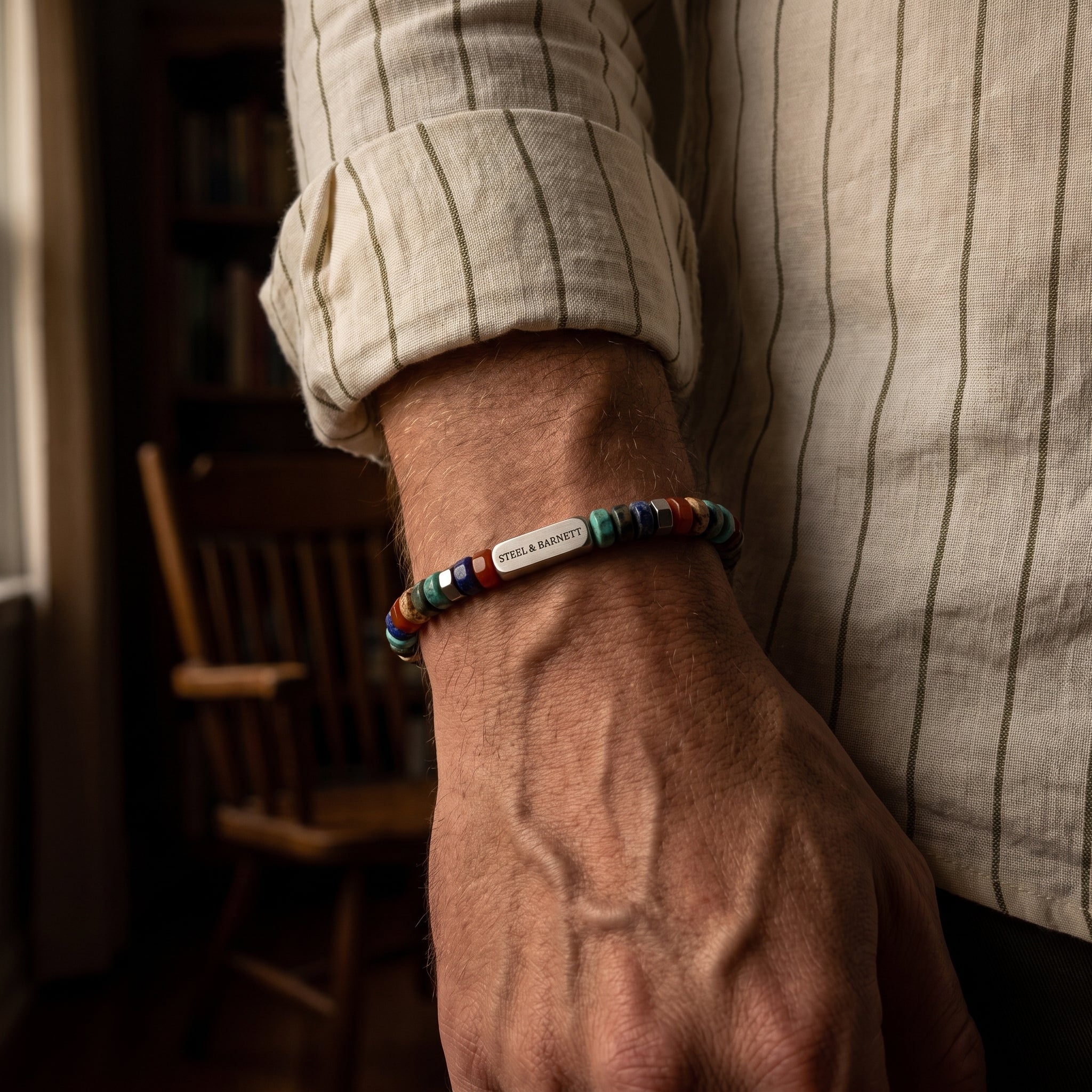 A close-up of a man's wrist wearing a colorful beaded bracelet with a silver metal logo bead