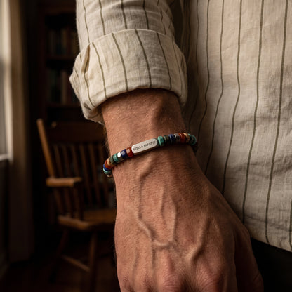 A close-up of a man's wrist wearing a colorful beaded bracelet with a silver metal logo bead