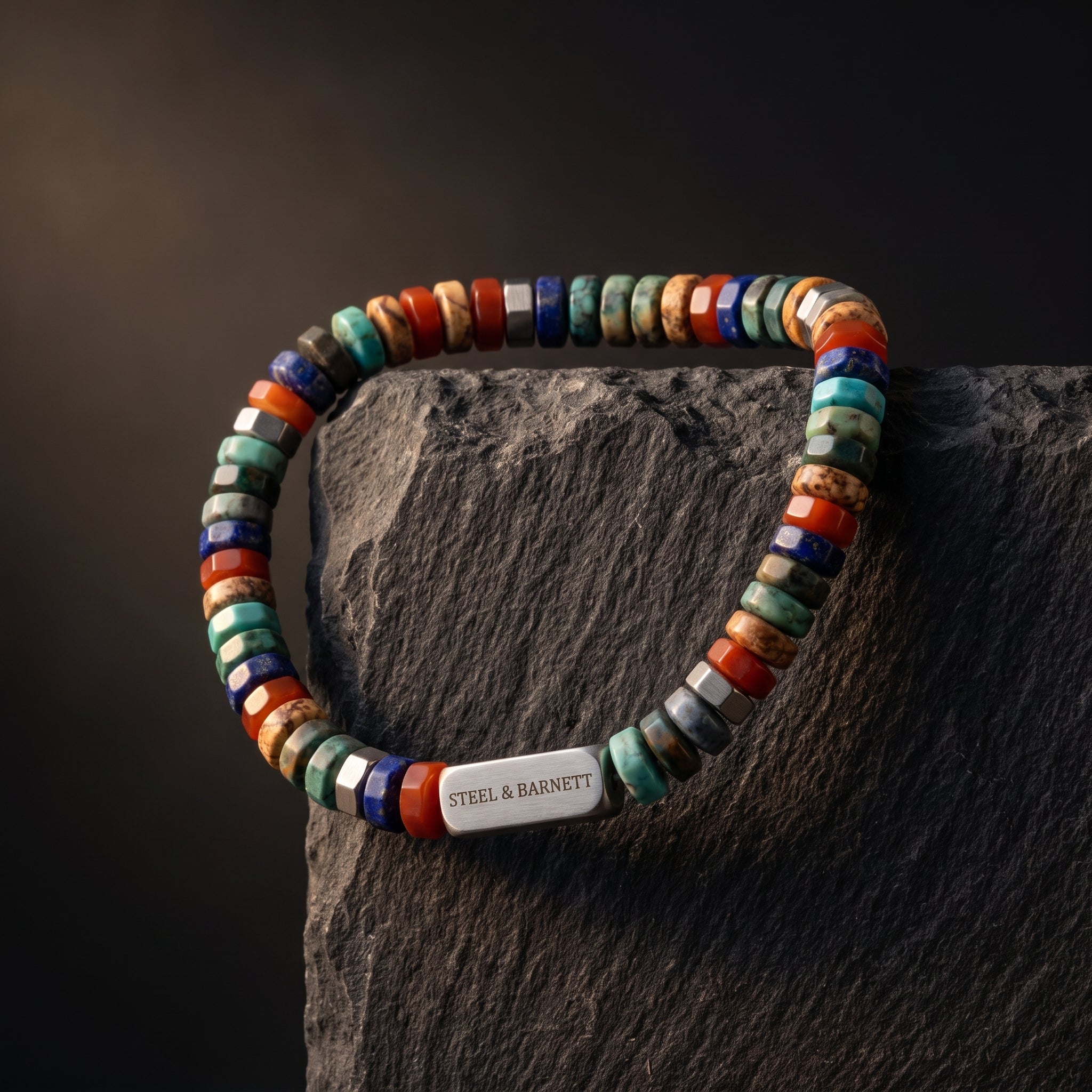 A beaded bracelet with a mix of colorful stone beads and a silver metal clasp engraved with 'STEEL & BARNETT', displayed on a dark textured rock against a dark background.