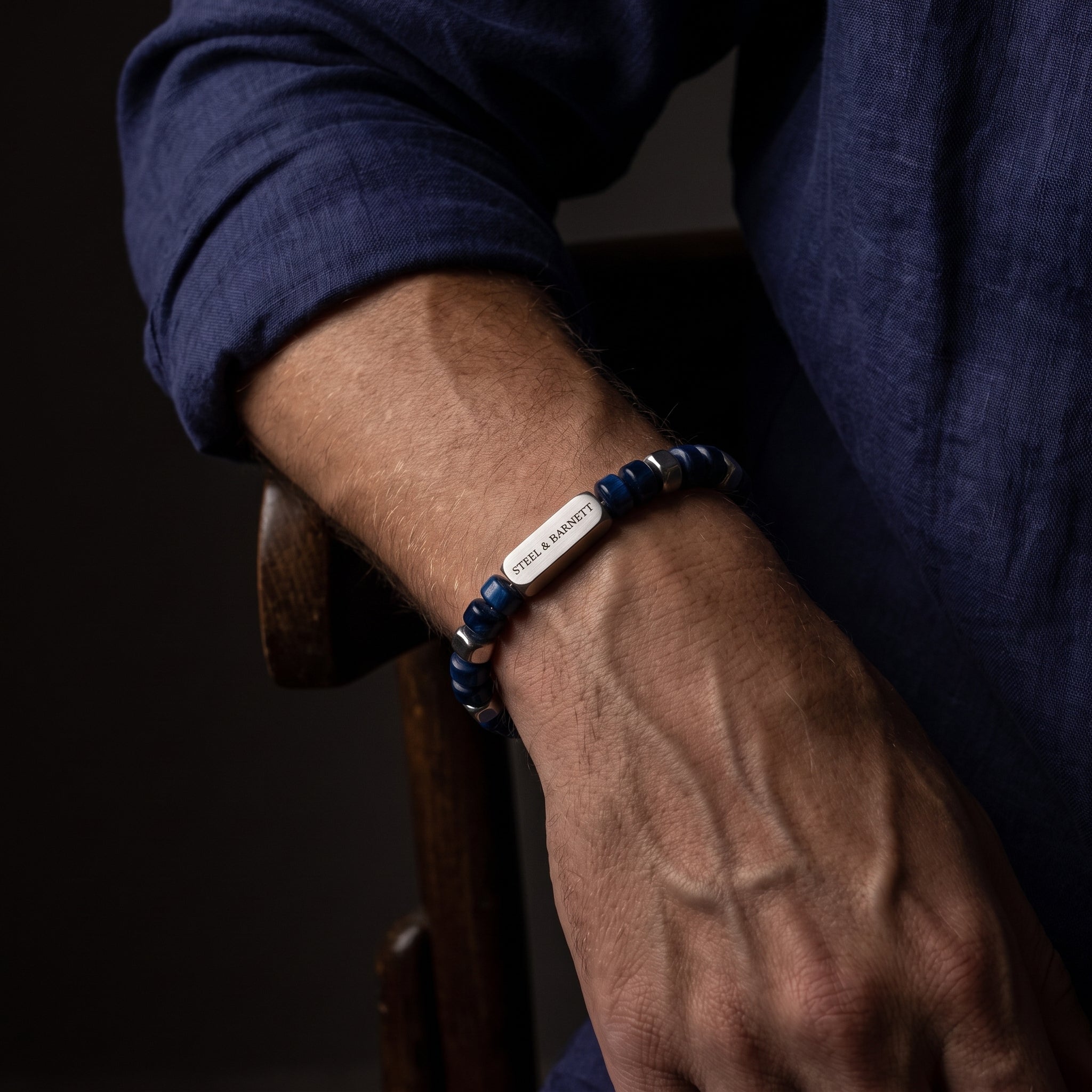 A close-up of a man's arm and hand wearing a beaded bracelet with sodalite dark blue beads.