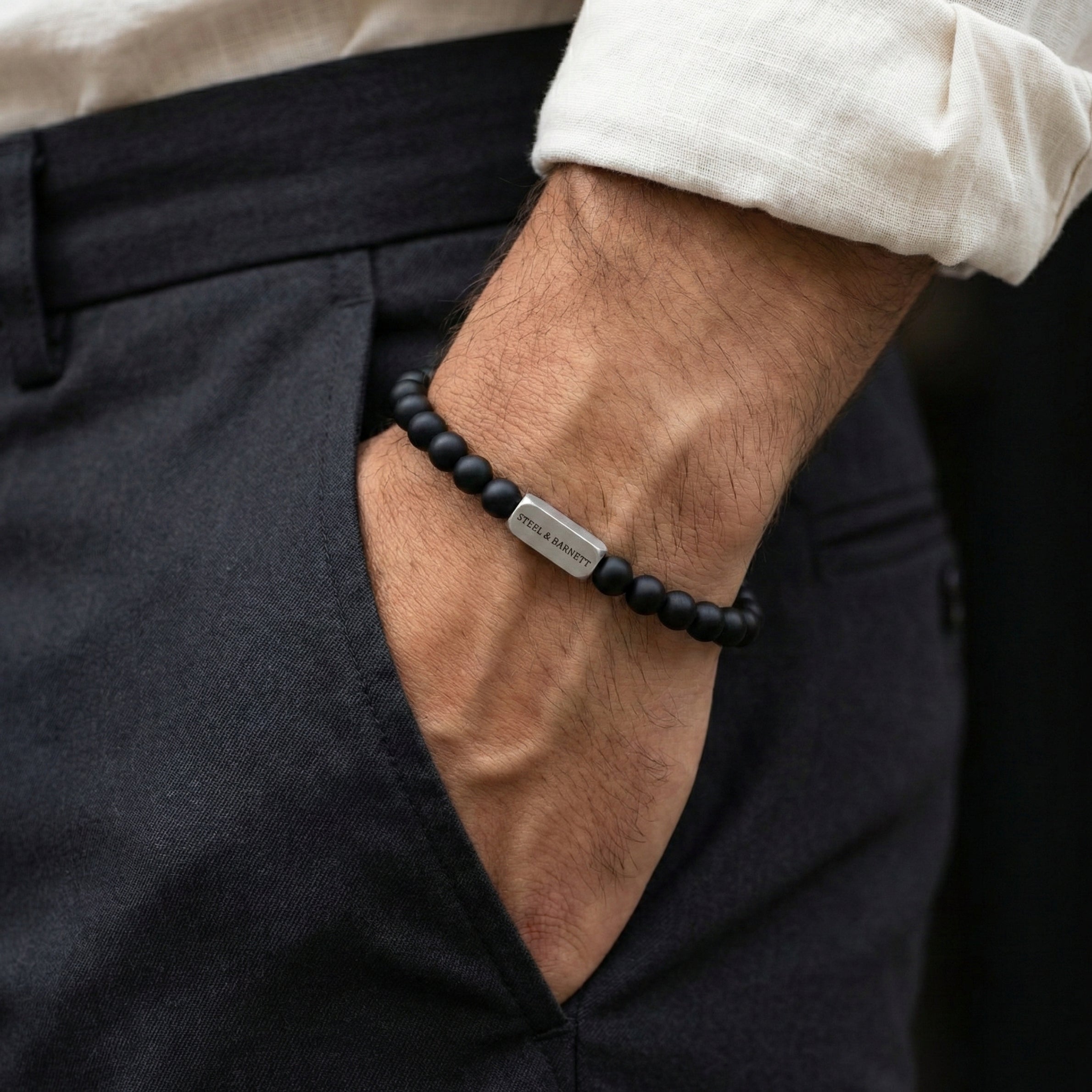 black beaded men’s bracelet with brushed stainless steel bar worn on wrist with hand in pocket
