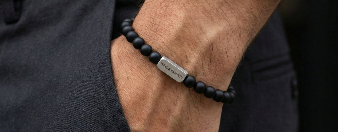 Black beaded bracelet with a metal tag on a wrist, worn with dark pants and a light shirt.