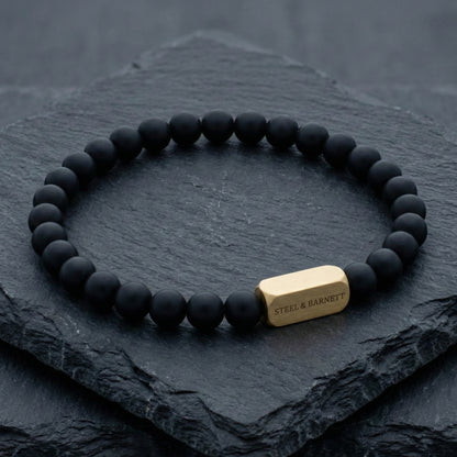 Black beads and plated 18K gold clasp on dark stone surface