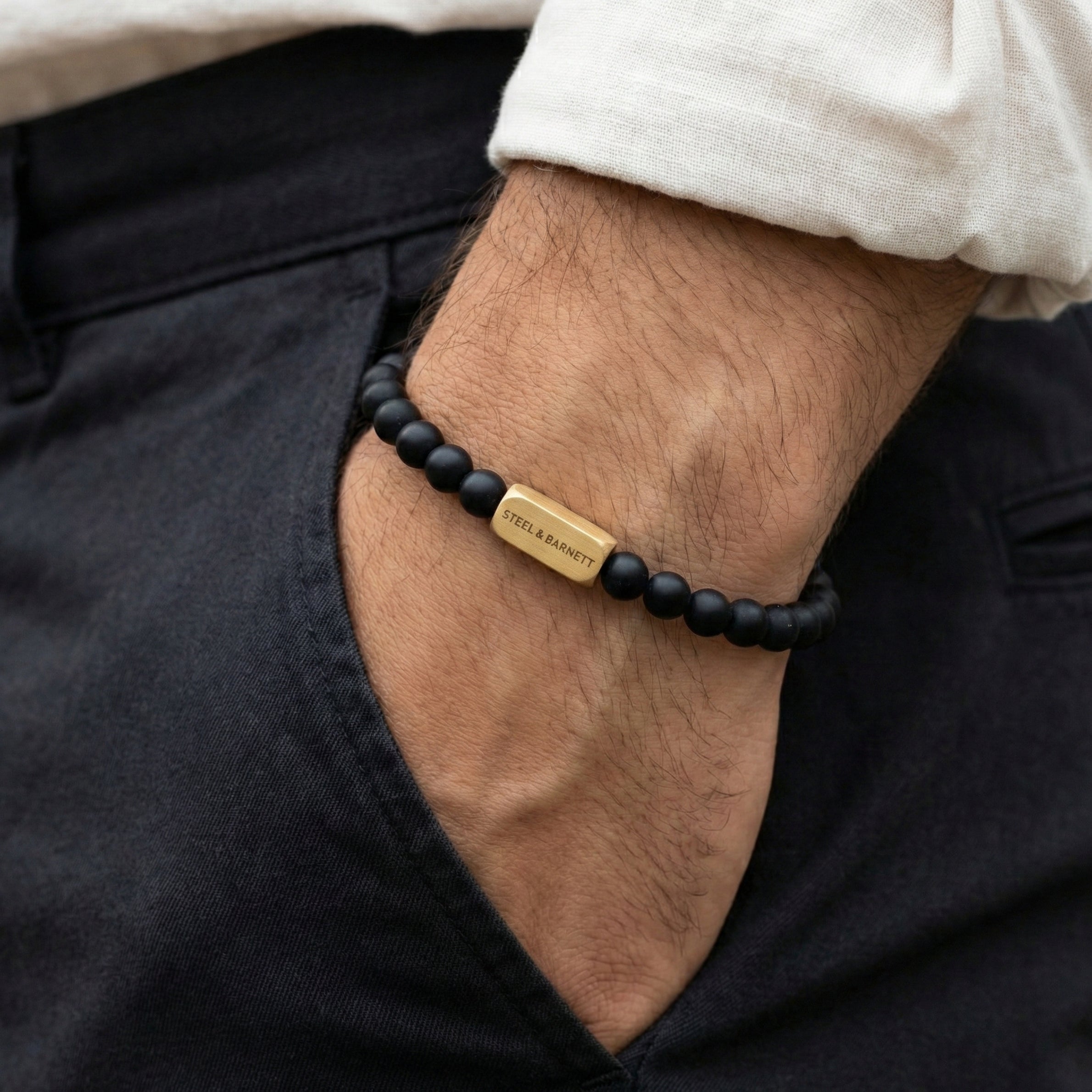 Black beaded men’s bracelet with matte beads and plated 18K gold clasp worn on wrist with hand in pocket