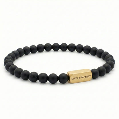 Black beaded men’s bracelet with matte round beads and plated 18K gold clasp on white background